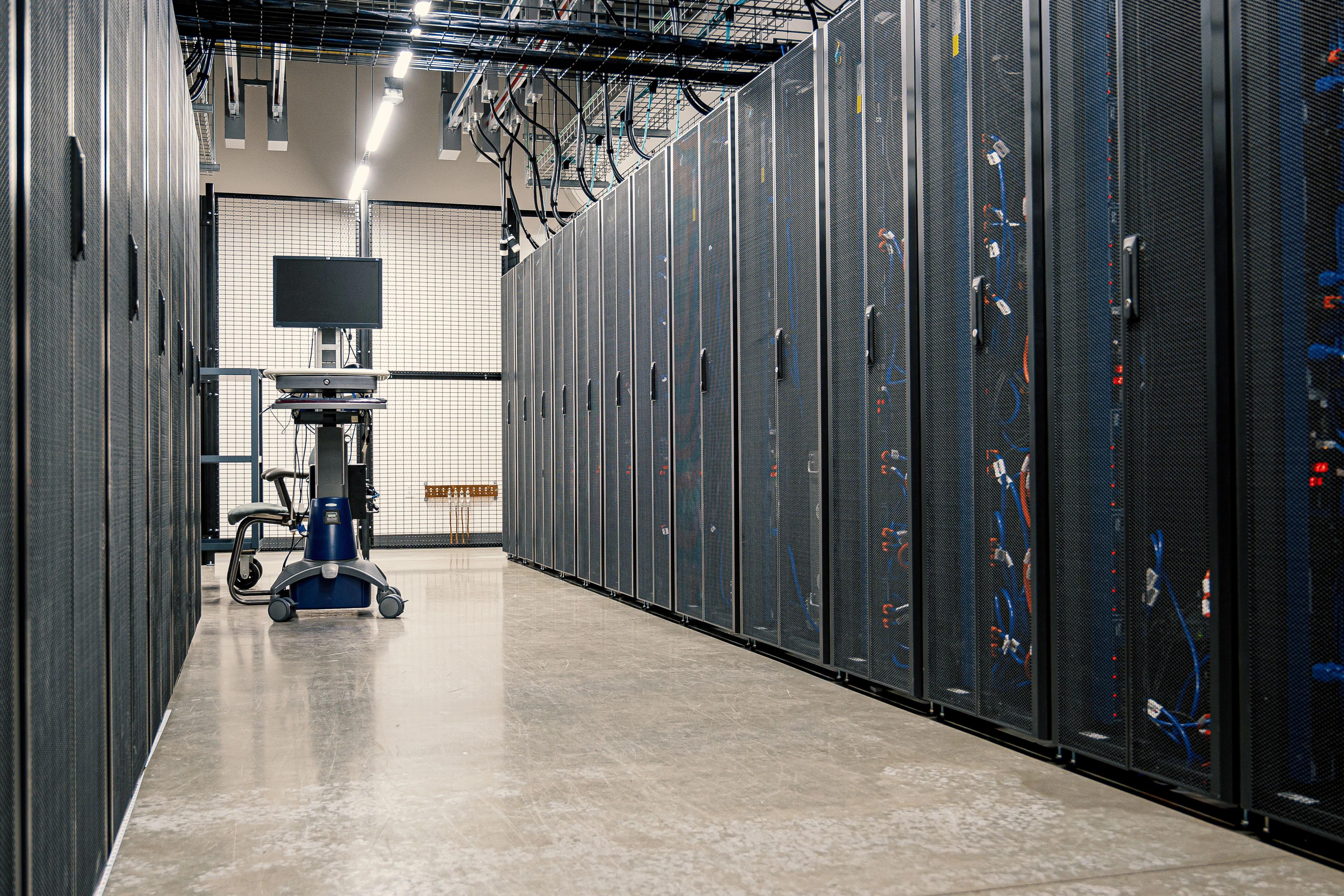 Rows of server racks and cabling in a data center, used as a general illustration of the physical infrastructure behind AI capacity.