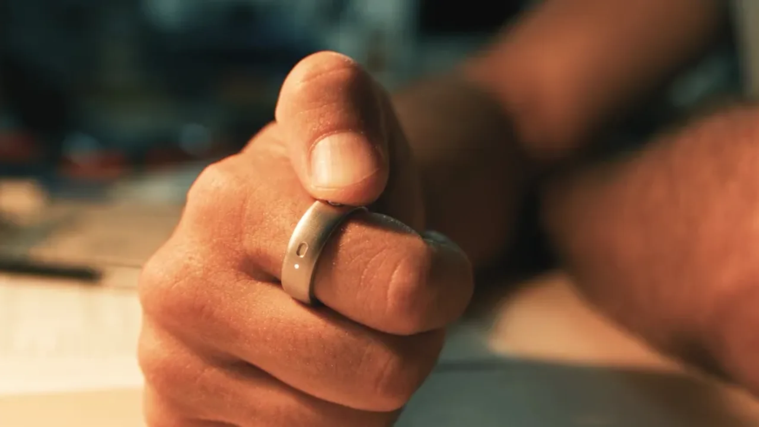 Close-up of a person pressing the button on a metallic Natura Interface ring worn on a finger, shown in the original launch image.